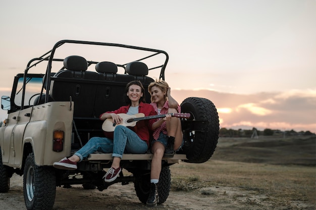 Smiley female friends traveling by car and playing guitar