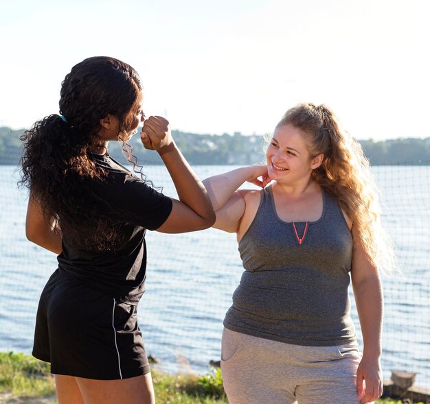 Smiley female friends trying the elbow greeting while working out outdoors