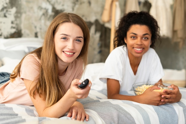 Smiley female friends watching tv in bed