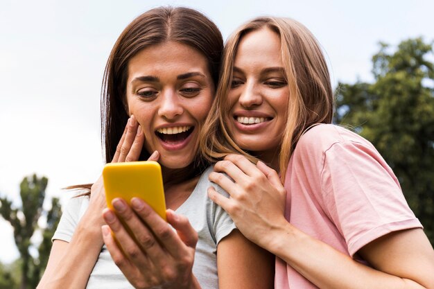 Smiley female friends with smartphone outdoors