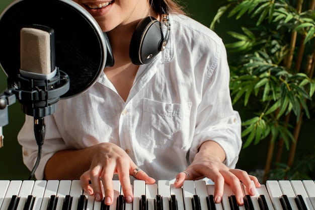 Smiley female musician playing piano keyboard indoors and singing into microphone
