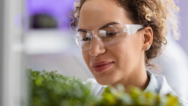 Smiley female researcher in the laboratory with safety glasses and plant