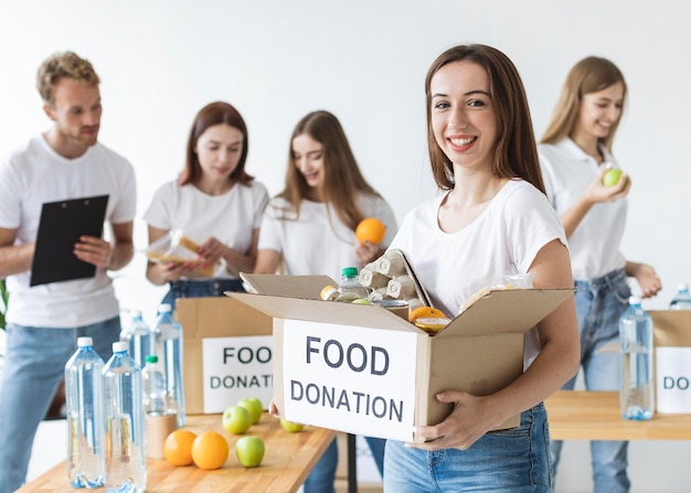 Смайлик-волонтер-женщина держит коробку с пожертвованиями на еду