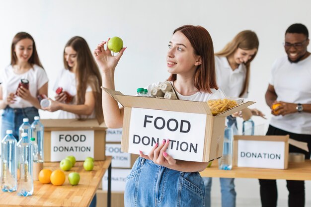 Smiley female volunteer holding food donations box with apple