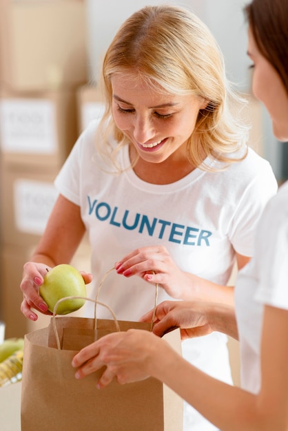 Free Photo smiley female volunteers putting food in bag for donation