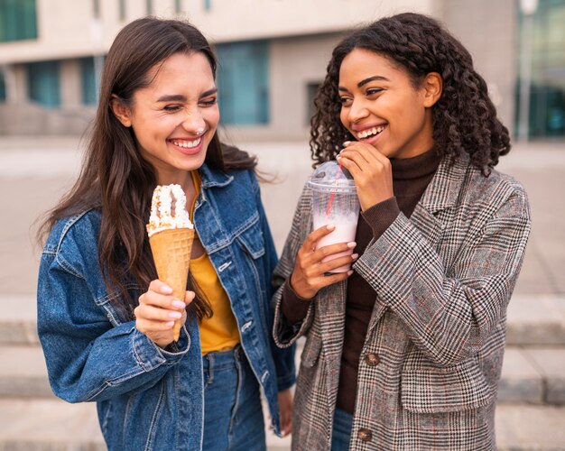 Бесплатное фото Улыбающиеся друзья пьют мороженое и молочные коктейли на улице