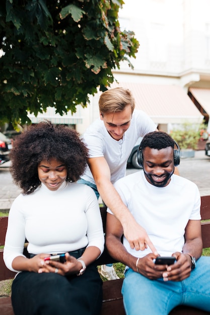 Smiley friends sitting on bench and using mobile