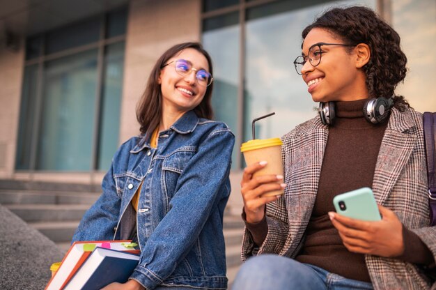 Smiley friends with books having coffee together outdoors