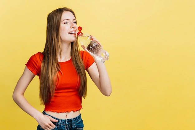 Foto gratuita ragazza di smiley che beve da una bottiglia di acqua con lo spazio della copia