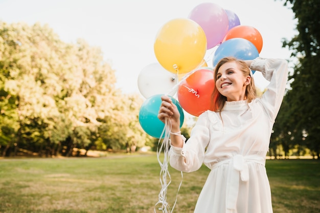 Улыбающаяся девушка в парке держит воздушные шары