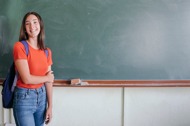 Smiley girl posing with backpack and blackboard