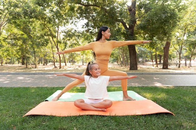 Foto gratuita ragazza sorridente e donna che fanno yoga a tutto campo
