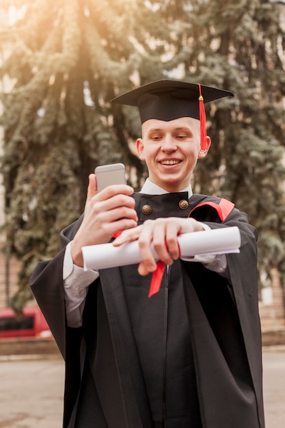 Foto gratuita ragazzo laureato di smiley con cellulare