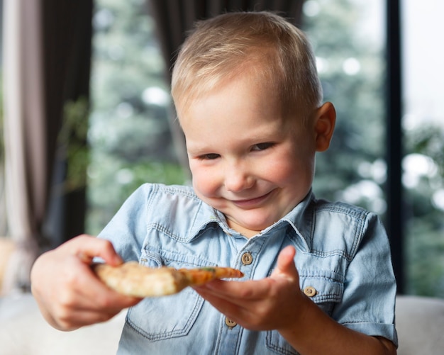 Foto gratuita fetta di pizza della holding del bambino di smiley