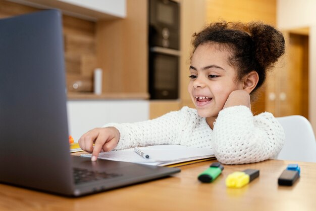 Smiley little girl at home during online school with laptop