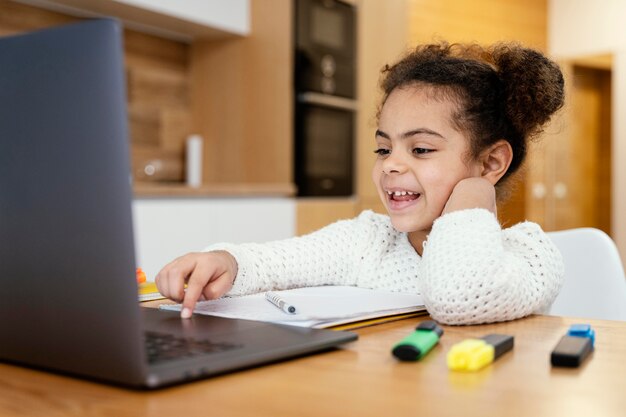 노트북으로 온라인 학교 동안 집에서 웃는 어린 소녀