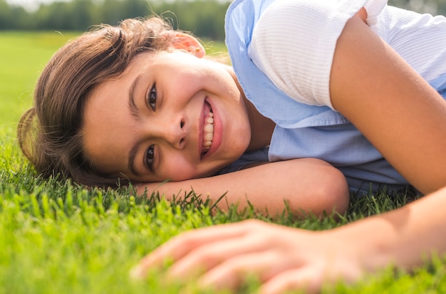 Улыбающаяся маленькая девочка смотрит в камеру, оставаясь на траве