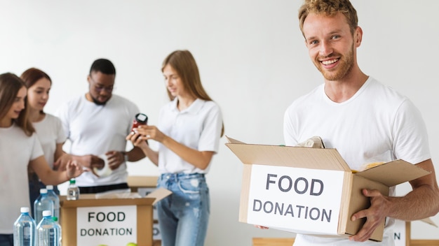 Смайлик-волонтер-мужчина держит коробку для пожертвований на еду