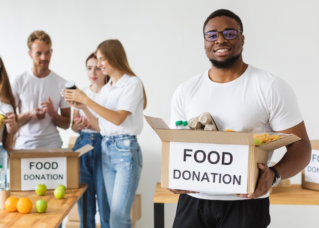Смайлик-волонтер-мужчина держит пожертвования на еду