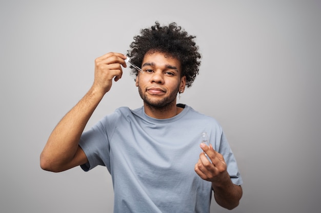 Smiley man applying face serum medium shot