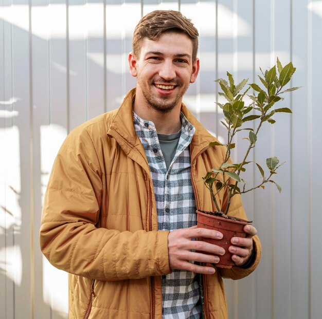 Free photo smiley man holding pot with small tree