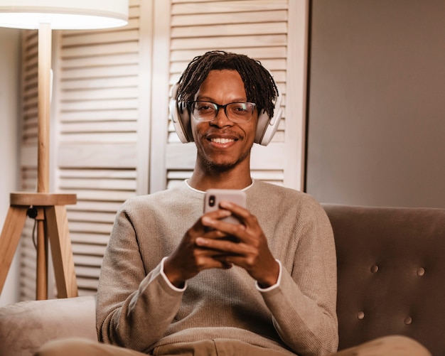 Free photo smiley man at home on the couch using smartphone and headphones