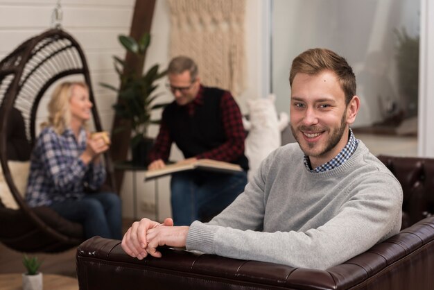 Smiley man posing on sofa with defocused parents