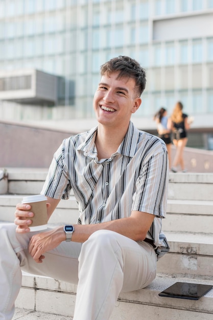 Smiley man sitting on steps outdoors while holding cup of coffee