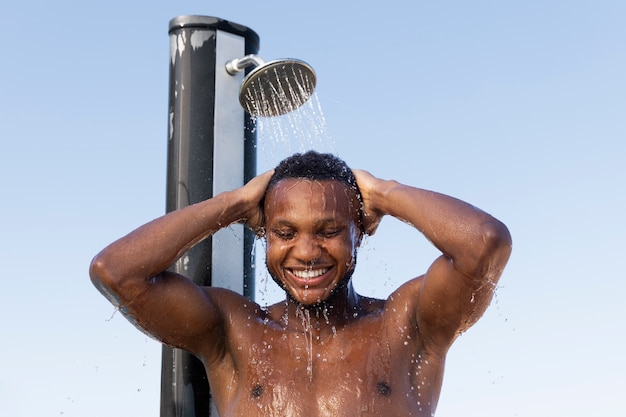 Free photo smiley man taking shower outdoors front view