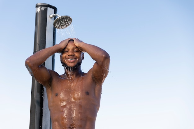 Free photo smiley man taking shower outdoors low angle