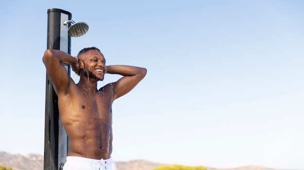 Smiley man taking shower outdoors side view