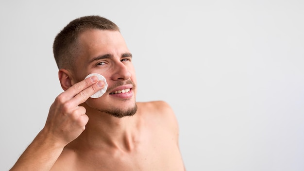 Smiley man using cotton pad on his face with copy space