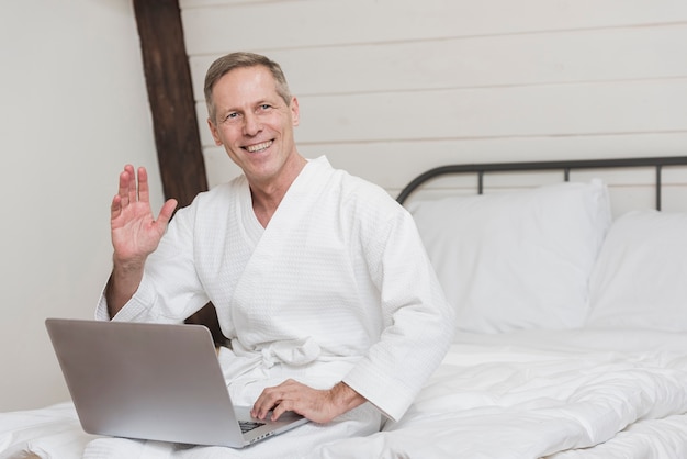 Smiley mature man holding a laptop in bed with copy space