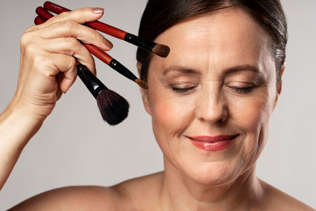 Smiley mature woman posing with make-up brushes