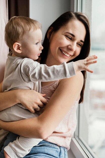 Smiley mother holding her child close to window