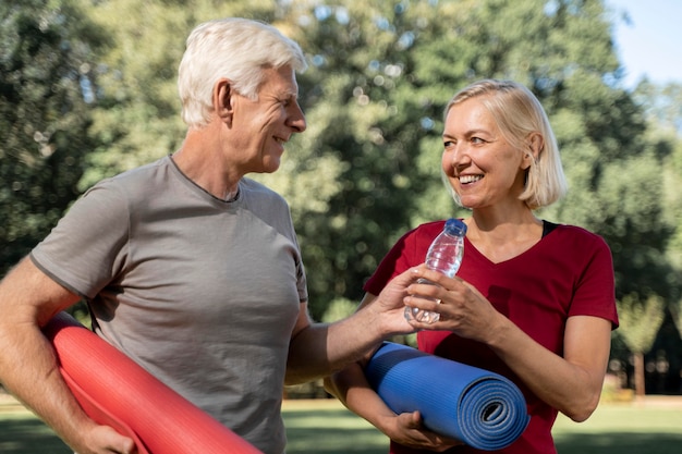 Smiley older couple outdoors with yoga mats and water bottle