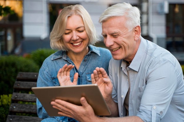 Smiley older couple waving at someone they're talking to on tablet