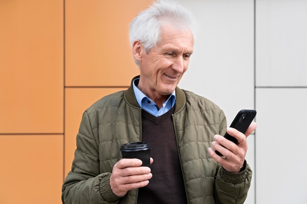 Smiley older man in the city using smartphone while having coffee