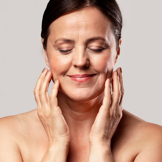 Smiley older woman with make-up on posing with hands on face