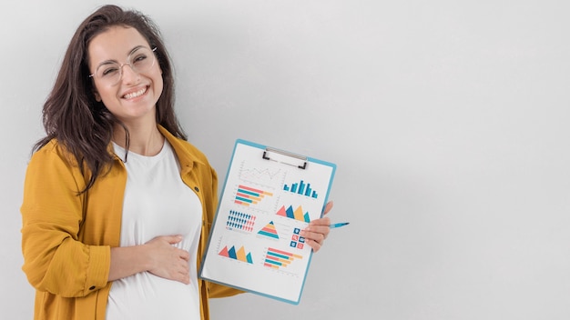 Free photo smiley pregnant woman holding clipboard and her belly