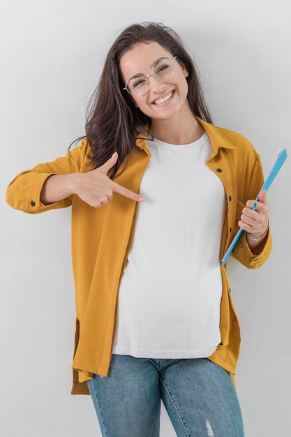 Free photo smiley pregnant woman holding clipboard and pointing down