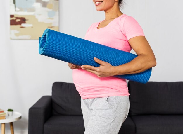 Smiley pregnant woman holding exercising mat