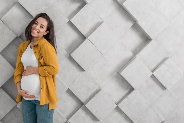 Smiley pregnant woman holding her belly with copy space