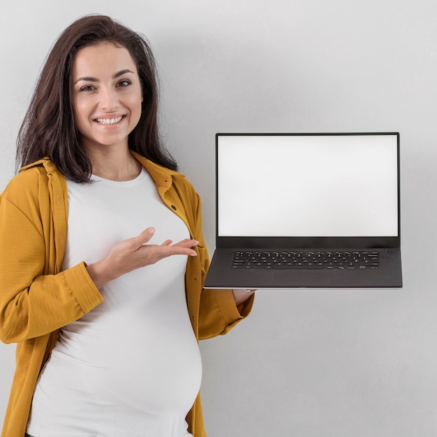 Smiley pregnant woman holding laptop and pointing at it