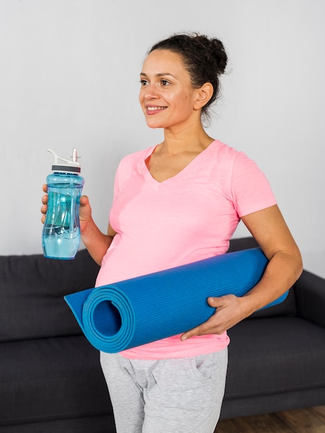 Smiley pregnant woman holding water bottle and mat