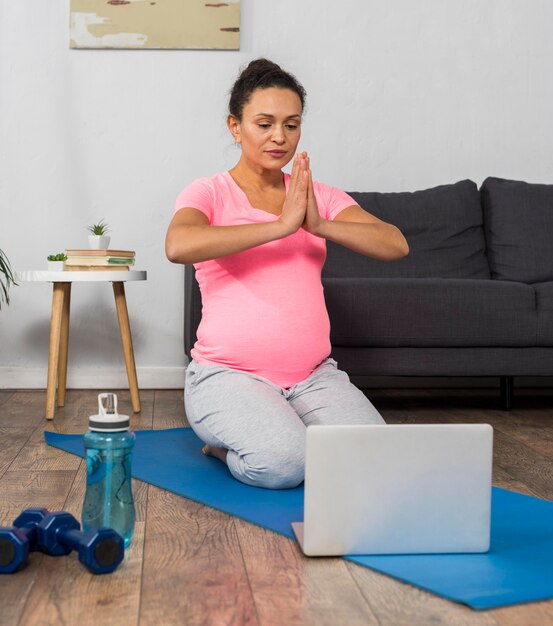 Smiley pregnant woman at home doing yoga with laptop