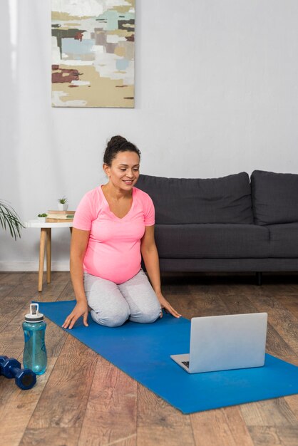 Smiley pregnant woman at home exercising with laptop