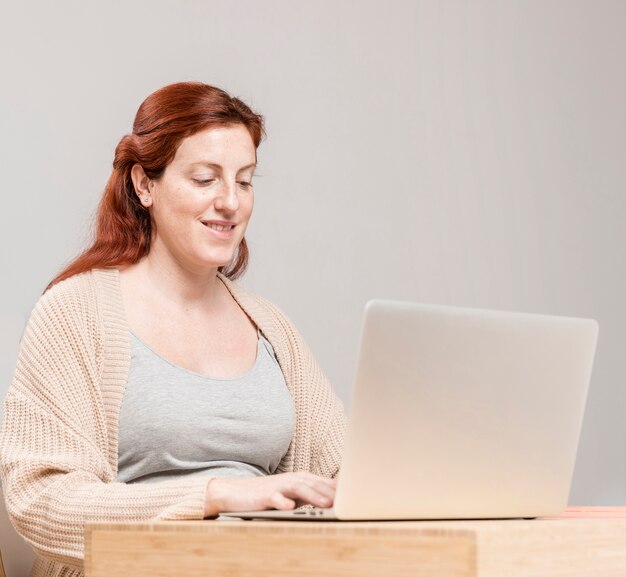 Smiley pregnant woman at home using laptop