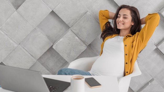 Free photo smiley pregnant woman looking at her laptop at home