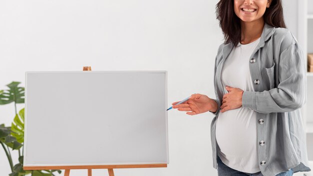 재택 근무하는 동안 화이트 보드를 보여주는 웃는 임신 한 여자